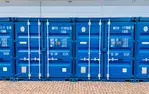 Drei blaue Frachtcontainer von Lager-Ein DE GmbH mit Beschriftungen, auf einem gepflasterten Boden vor einem Gebäude.