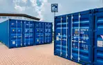 Blaue Frachtcontainer auf gepflastertem Gelände bei Lager Ein DE GmbH in Schwülper. Sichtbar sind Gebäudeteil und Schilder.