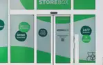 Außenansicht eines Storebox-Standorts mit grüner Fensterfolie, beschriftet mit Einfach & Sicher, Ohne Kaution und 24/7 Zugang.