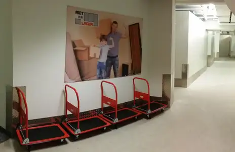 Lagerraum bei Miet Dein Lager in Winnenden mit roten Transportwagen und Werbeposter im Flur.