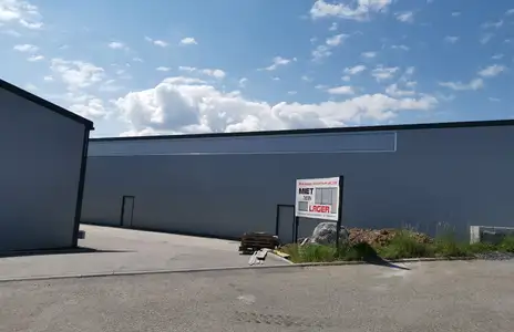 Außenansicht von Miet dein Lager Schwabbach mit grauem Gebäude und Zufahrt bei sonnigem Himmel. Schild mit Aufschrift Miet dein Lager.