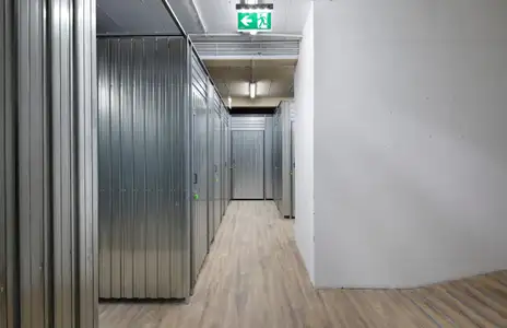 Gang mit Metall-Lagerräumen bei Storebox in Freiburg. Notausgangsschild an der Decke, Holzboden.