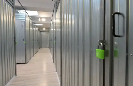 Innenansicht von Storebox in Osnabrück mit abschließbaren Metallkabinen und grünem Vorhängeschloss auf hellem Holzboden.