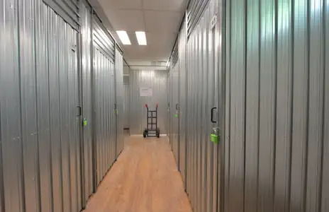 Innenansicht bei Storebox Osnabrück: Metallene Lagertüren im Gang, Holzboden, Transportkarre im Hintergrund.