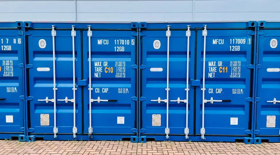 Drei blaue Frachtcontainer von Lager-Ein DE GmbH mit Beschriftungen, auf einem gepflasterten Boden vor einem Gebäude.