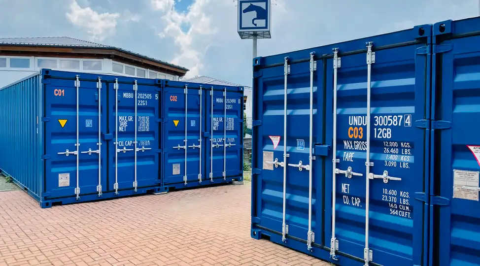 Blaue Frachtcontainer auf gepflastertem Gelände bei Lager Ein DE GmbH in Schwülper. Sichtbar sind Gebäudeteil und Schilder.